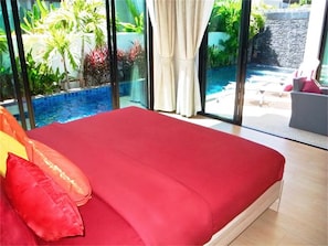 Une chambre dotée d’un grand lit, offrant une vue sur une piscine, et donnant sur une zone extérieure grâce à une porte vitrée.