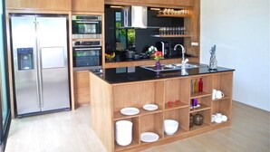 A modern kitchen with wooden cabinets, stainless steel appliances, and a central island with a sink. - Baan Bua Nai Harn 3 bedrooms Villa (Rawai)