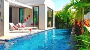 A modern pool area with lounge chairs and a clear blue pool, surrounded by tropical plants. - Baan Bua Nai Harn 3 bedrooms Villa (Rawai)