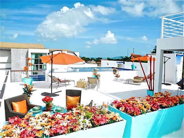 A rooftop pool area with lounge chairs, umbrellas, and flower arrangements.