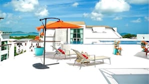 A rooftop terrace with a pool, lounge chairs, and a large orange umbrella.