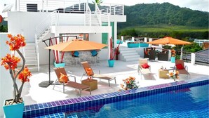 A modern outdoor pool area with lounge chairs and umbrellas, a staircase leading to an upper level, and a view of a green landscape.