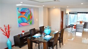 A modern dining area with a glass table, dark wooden chairs, and a colorful abstract painting on the wall.