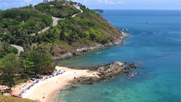 A coastal landscape with a winding road, a sandy beach, and clear turquoise waters.