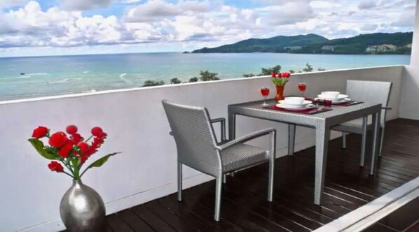 Een balkon met een tafel gedekt voor twee personen, stoelen en een vaas rode bloemen.