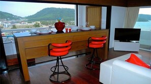 Een moderne keuken met uitzicht op een stad en bergen, twee rode barkrukken, een witte bank en een flatscreen televisie.
