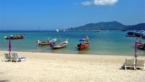 A beach with several boats anchored near the shore, a clear blue sky, and a distant mountain range.