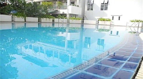 A swimming pool with a tiled edge, surrounded by a white building with balconies.