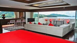 A modern living room with a large red sofa, a TV, and a balcony with a view of the sea.