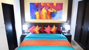 Une chambre d’hôtel avec un grand lit, des oreillers aux couleurs vives et un tableau éclatant accroché au-dessus du lit.