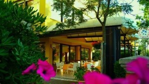 Un hotel moderno con un área de estar al aire libre techada, rodeado de exuberante follaje y flores vibrantes.