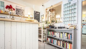 Un interior moderno y bien iluminado con un mostrador de madera, una estantería llena de libros y elementos decorativos como flores y un letrero de pizarra.