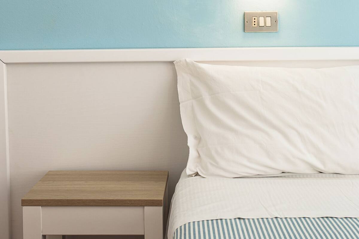 A bedroom with a bed, a bedside table, and a wall-mounted light fixture.