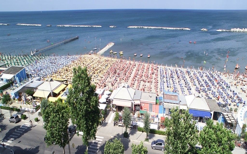 A beach with rows of sunbeds and umbrellas, a pier in the background, and buildings along the shore.