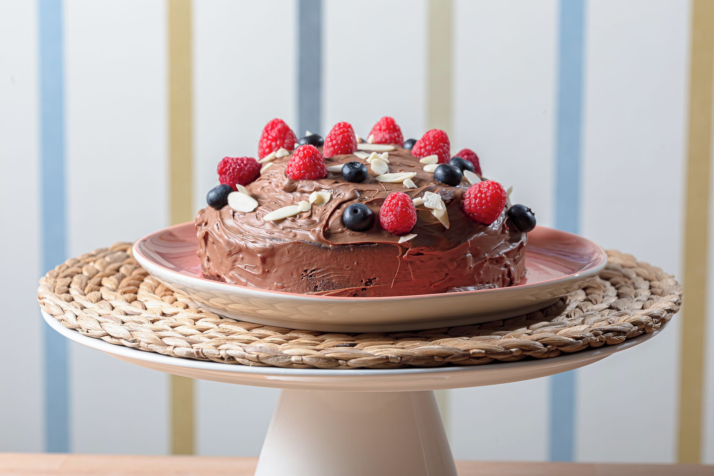 Un pastel de chocolate con frambuesas y arándanos sobre un pedestal blanco para pasteles.