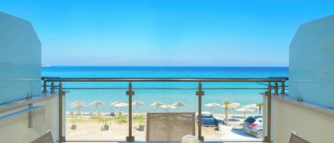 A balcony with a view of the beach, outdoor seating, and umbrellas.