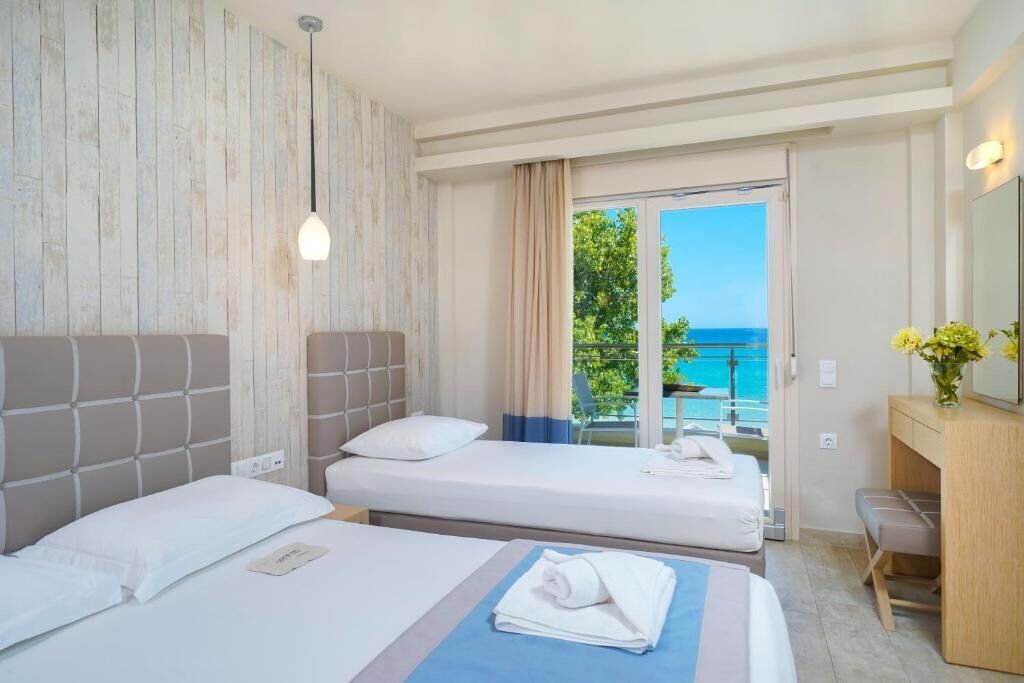 Habitación de hotel con dos camas, baño y balcón con vista al mar.