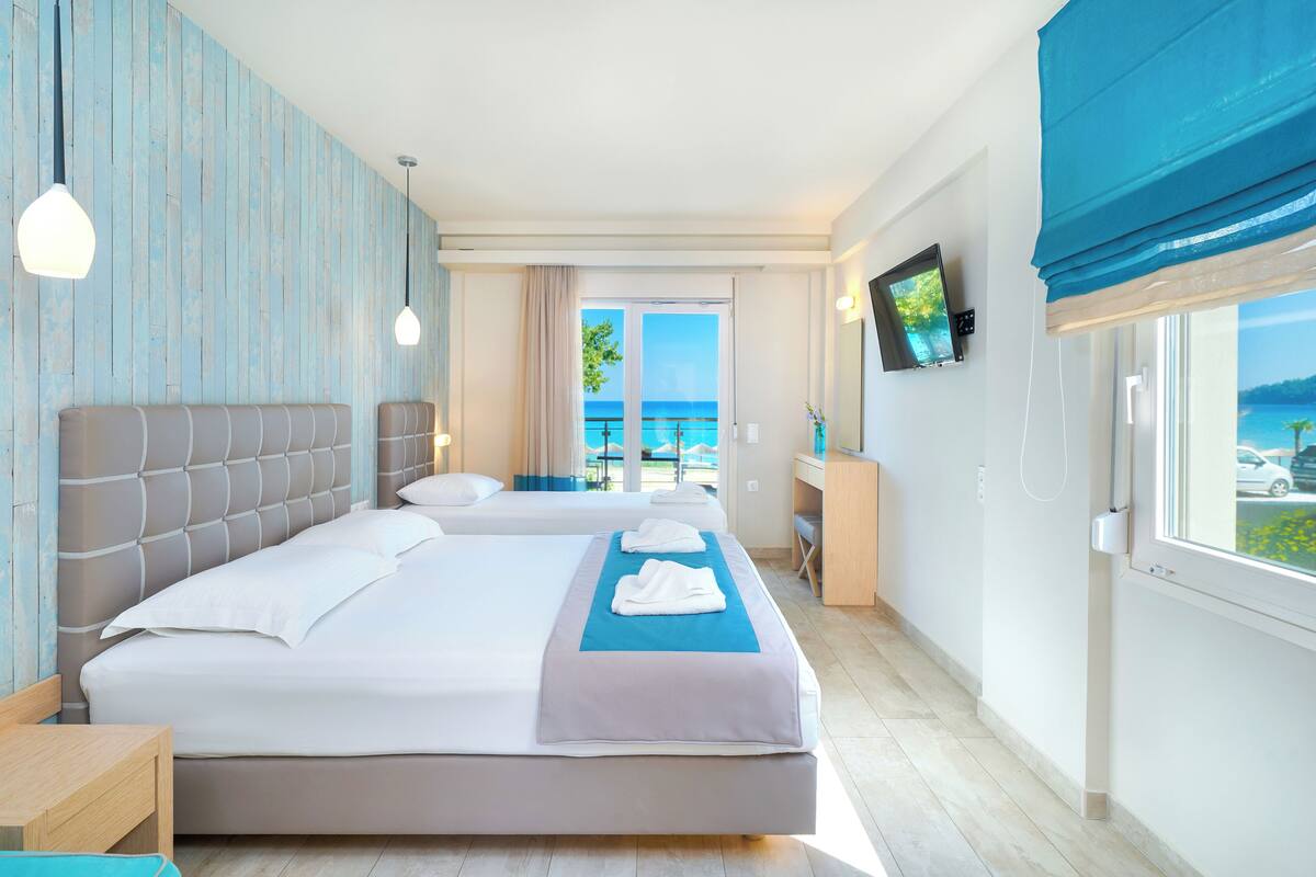 Habitación de hotel con dos camas, un escritorio, un televisor y un balcón con vista al mar.