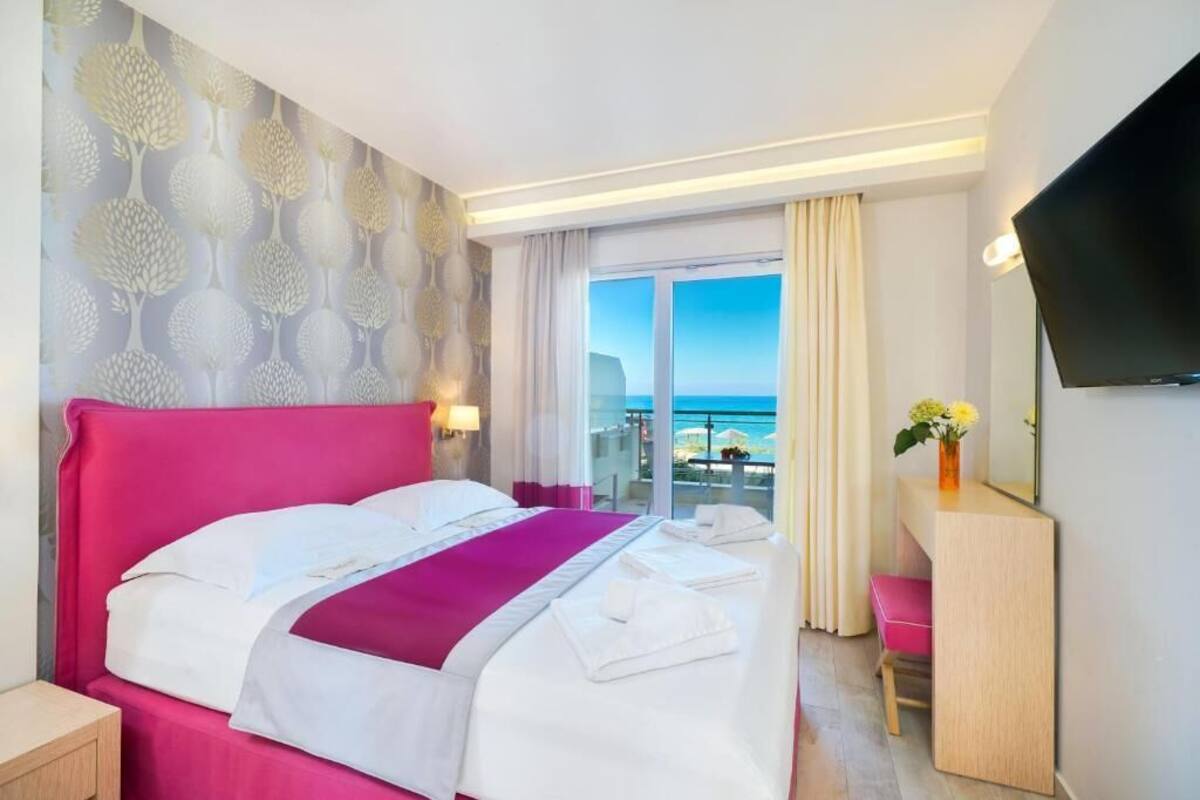 Una habitación de hotel con una cama grande, un escritorio, un televisor y un balcón con vistas al mar.