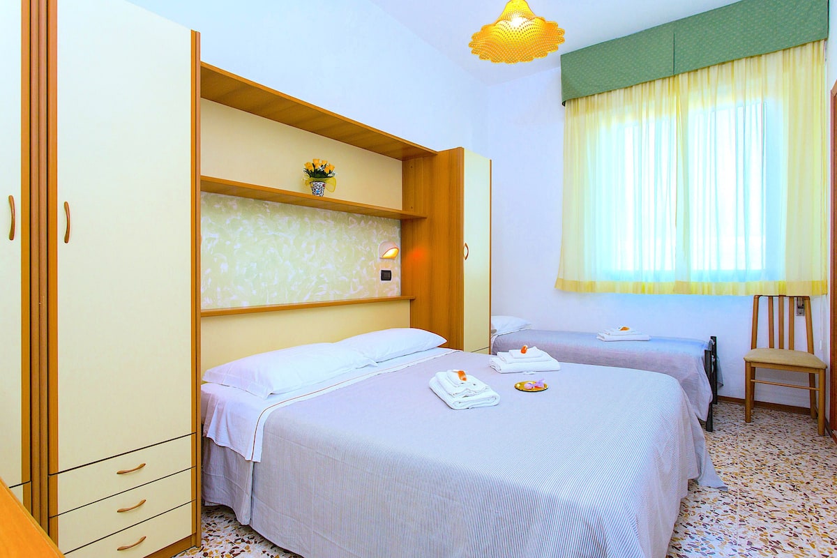 A hotel room with two beds, a wardrobe, a chair, and a window with curtains.