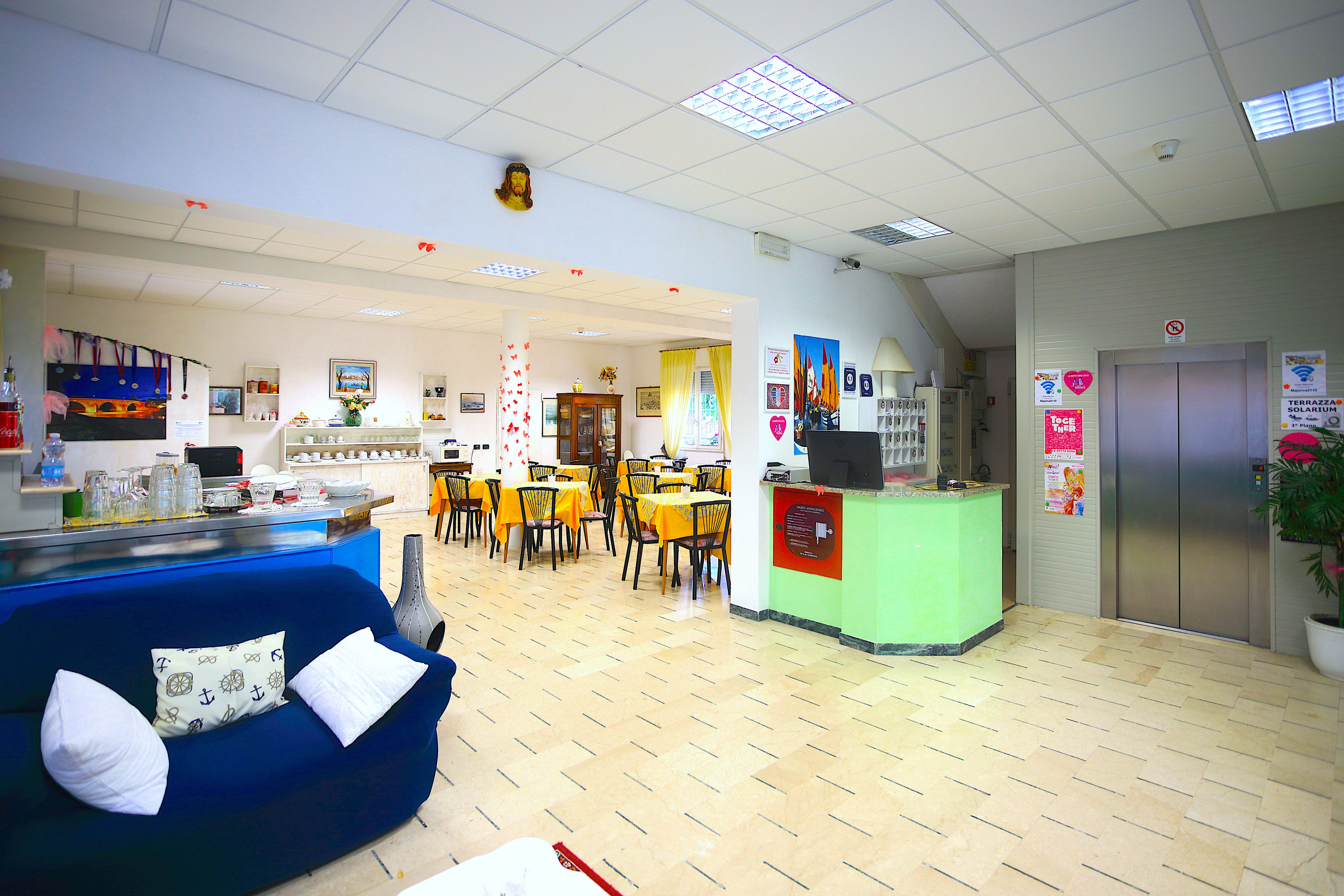 A hotel lobby with a reception desk, a blue sofa with white cushions, yellow tables, and a green counter.