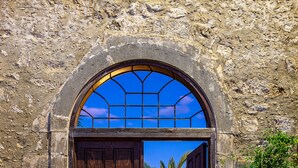 An arched stone doorway leading to a courtyard with a palm tree and a lamp post. - Villa Candice (Rethymno)