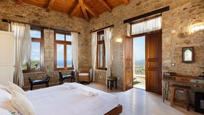 A spacious bedroom with a large bed, wooden furniture, stone walls, and a view of the landscape. - Villa Candice (Rethymno)