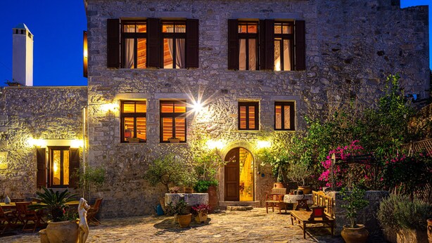 A stone building with multiple windows, a courtyard with outdoor seating, and potted plants. - Villa Candice (Rethymno)
