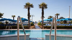 Ein Swimmingpool mit blauen Sonnenschirmen und Palmen.