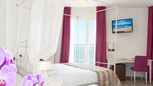 Ein Hotelzimmer mit Himmelbett, Schreibtisch, Stuhl, Fernseher und einem Fenster mit Vorhängen.