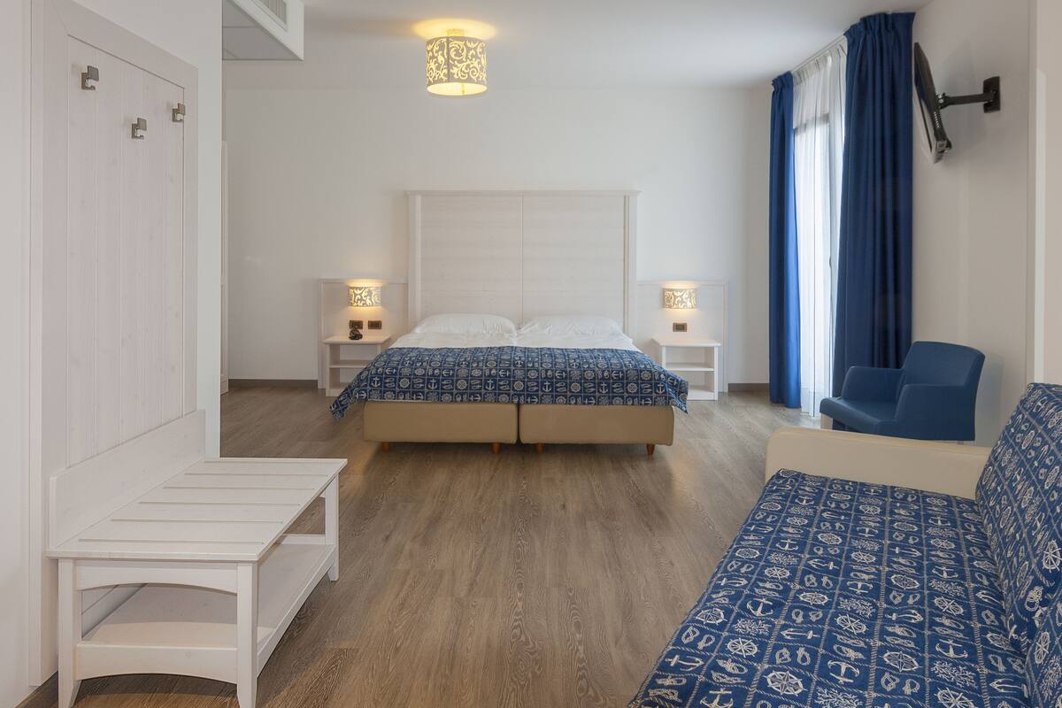 A bedroom with a bed, bedside tables, a bench, a sofa, and a ceiling light fixture.