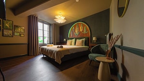 A bedroom with a bed, a side table, a chair, a window, and a wall with framed pictures. - Buitenplaats Kasteel Elsloo (Elsloo)