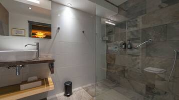 Un baño moderno con ducha envuelta en vidrio, lavamanos con encimera de madera y espejo sobre el lavamanos.