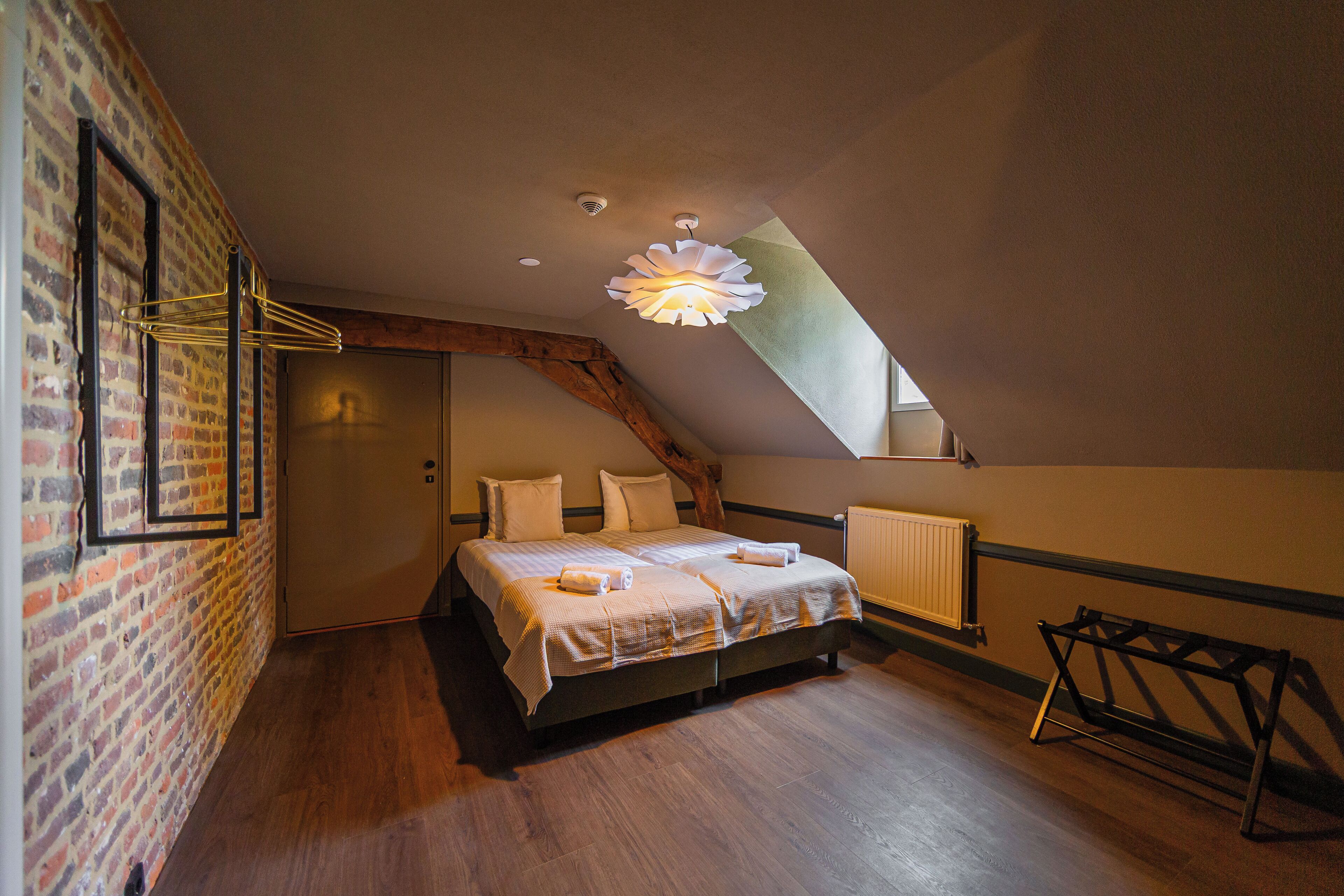 A bedroom with a sloped ceiling, a bed with linens, a wooden floor, and a brick wall.