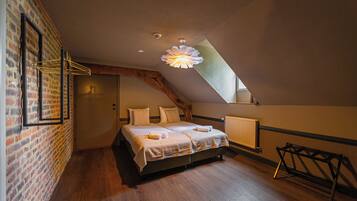 A bedroom with a sloped ceiling, a bed with linens, a wooden floor, and a brick wall.