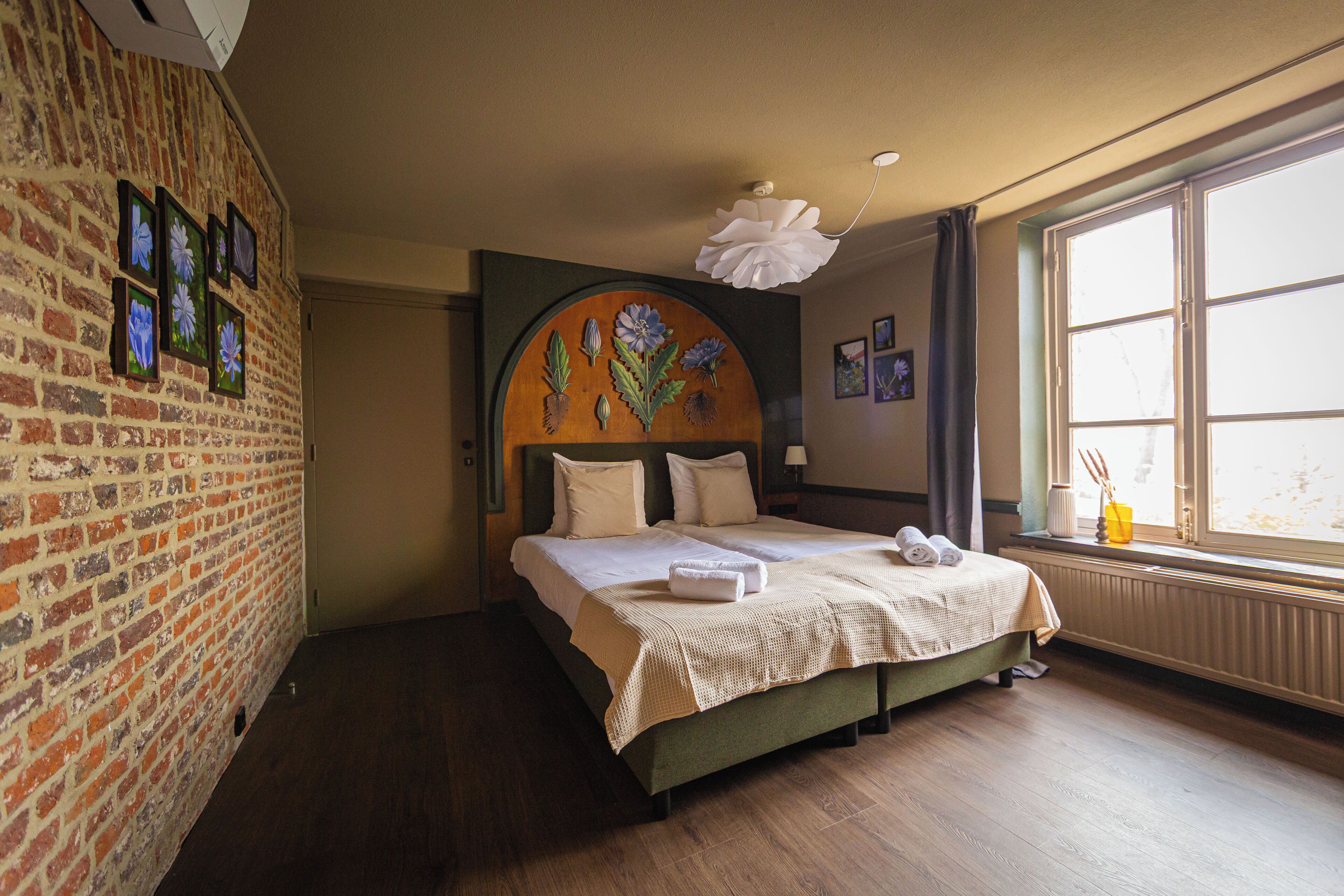 Ein Hotelzimmer mit Backsteinwand, großem Fenster und einem Bett mit Blumenbordell.
