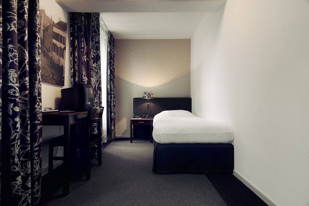Une chambre d’hôtel comprenant un lit, un bureau, une chaise, une table de chevet, une lampe et un tableau accroché au mur.