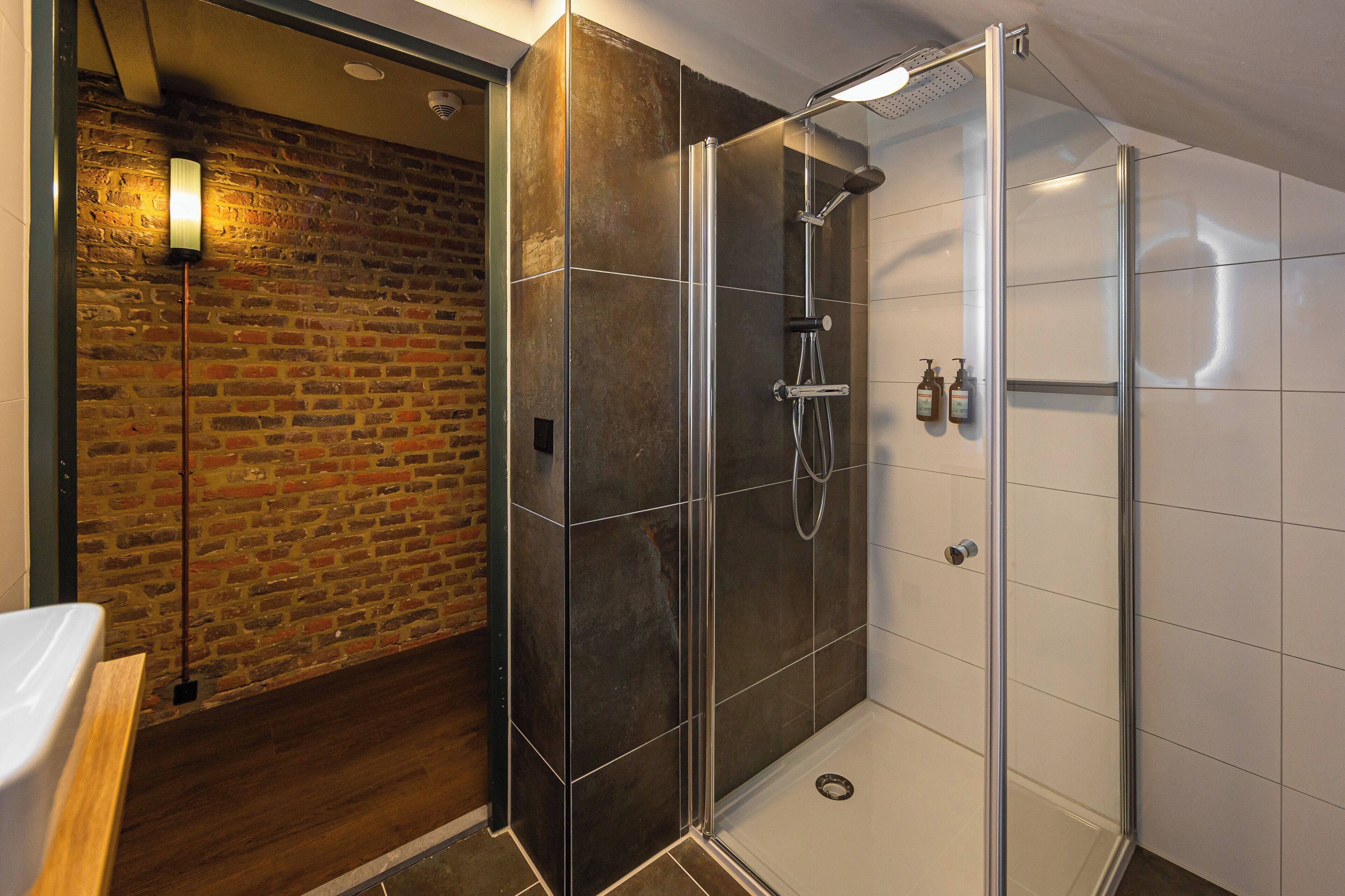 A modern bathroom with a glass-enclosed shower, a brick wall, and a wooden floor.