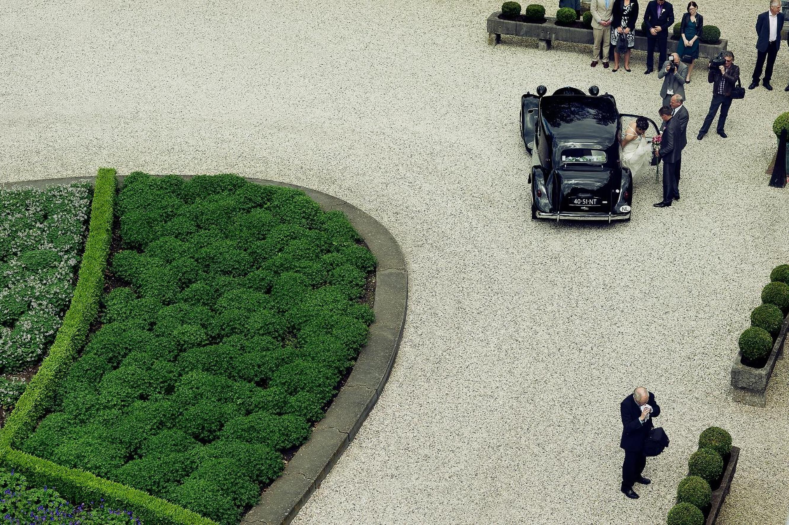 Un entorno exterior elegante con un coche negro, un jardín cuidado y varias personas.