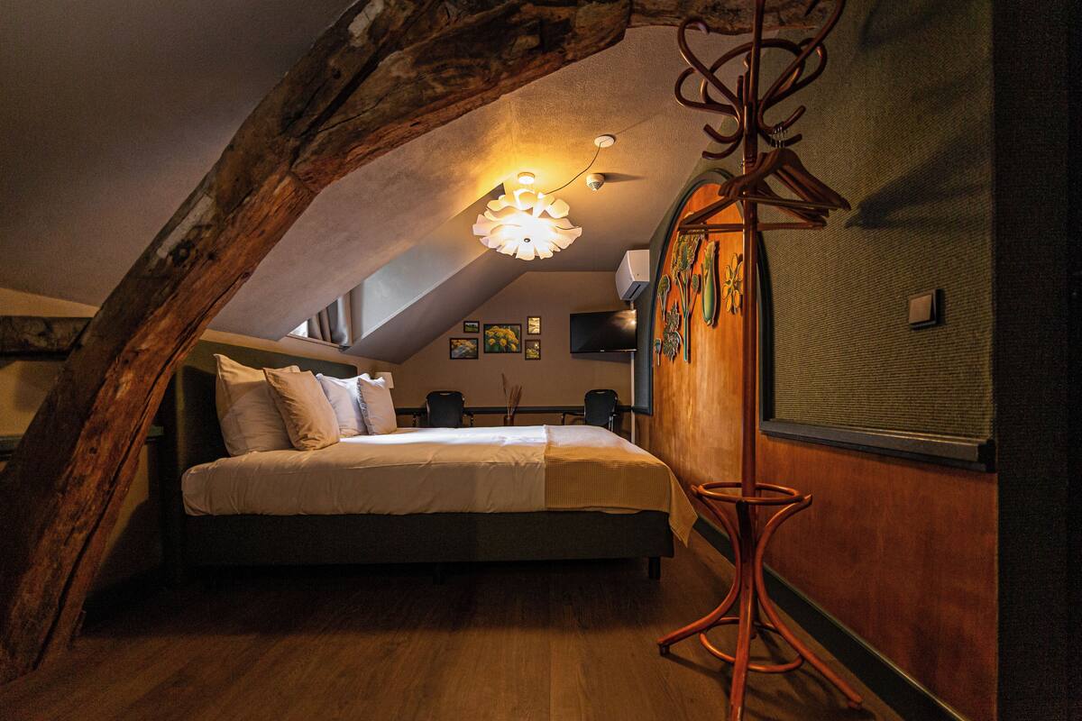 Une chambre avec un plafond en pente, un lit, un luminaire suspendu et un porte-manteau.