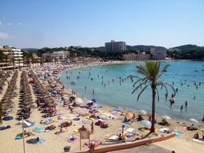 Ein überfüllter Strand mit vielen Sonnenschirmen und Menschen, die das Wasser genießen.