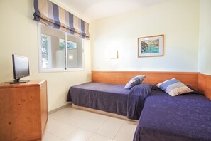 Ein Zimmer mit zwei Betten, einem Holzschrank, einem Fernseher, einem Fenster mit Vorhängen und einem gerahmten Bild an der Wand.