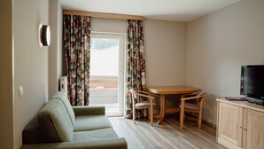 Una sala pequeña con un sofá, una mesa y dos sillas, un televisor y un ventanal con cortinas.