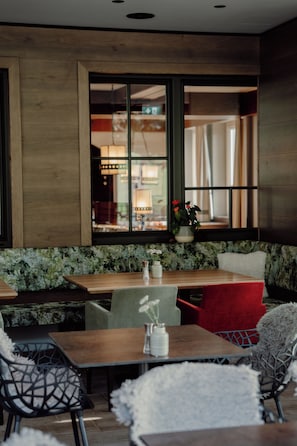 A restaurant interior with wooden tables and chairs, a large window with a view of the street, and a green cushioned bench. - Das Filzmoos (Filzmoos)