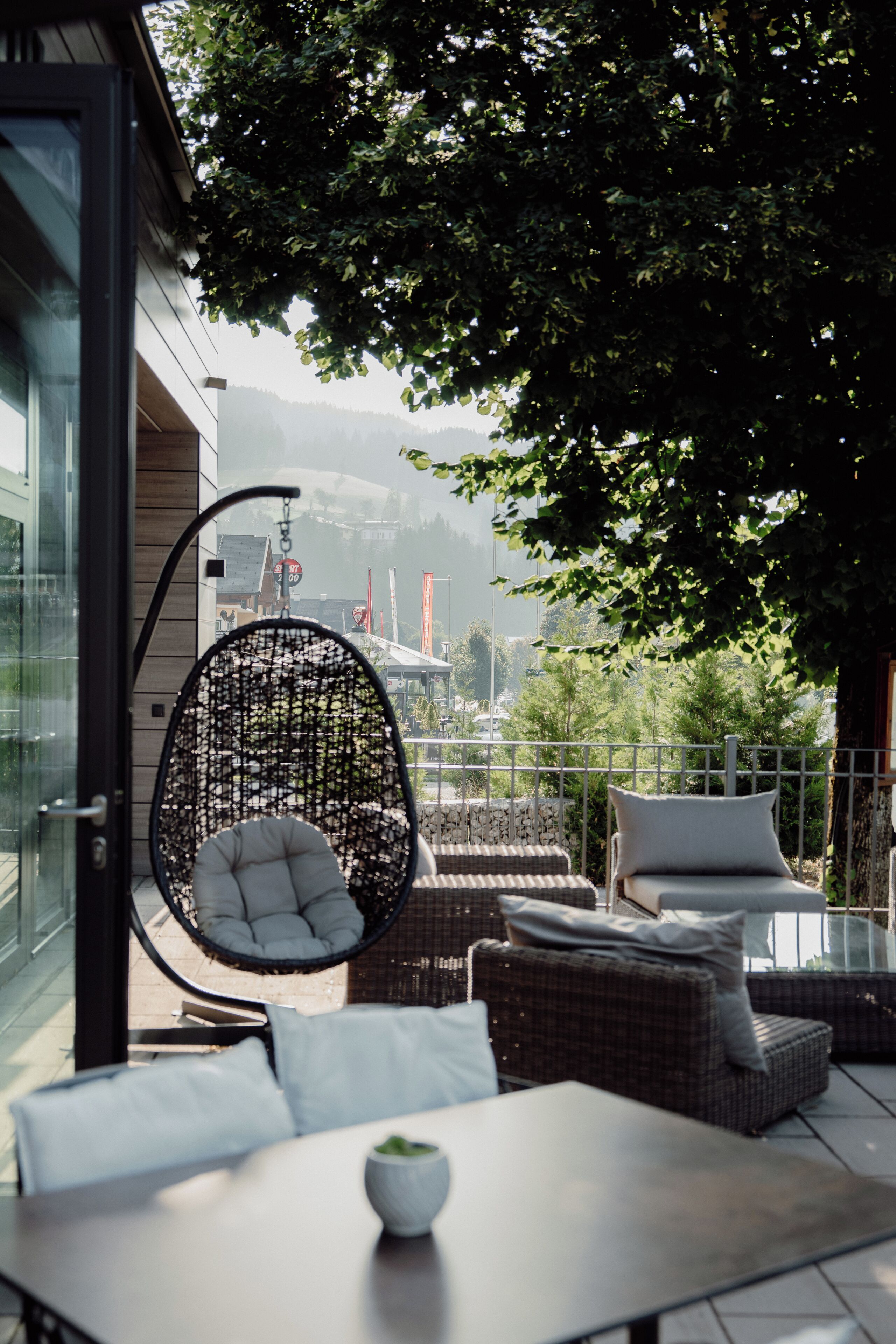 A modern outdoor seating area with a wicker chair, cushioned sofas, and a table with a bowl of greenery.