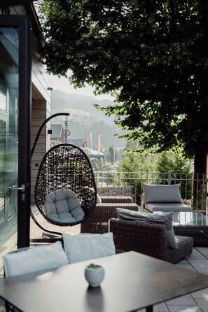 A modern outdoor seating area with a wicker chair, cushioned sofas, and a table with a bowl of greenery. - Das Filzmoos (Filzmoos)