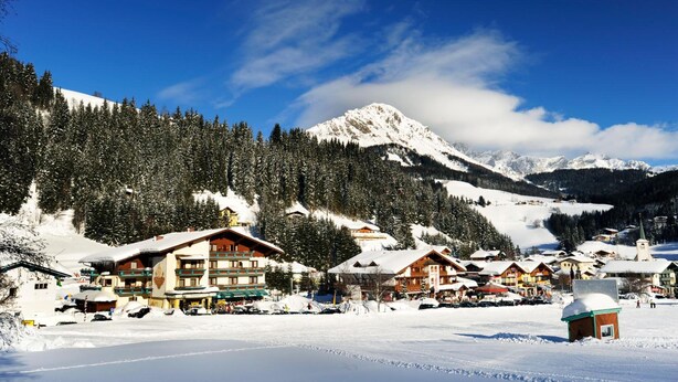 A snow-covered mountain village with traditional wooden buildings, a ski resort, and a clear blue sky. - Das Filzmoos (Filzmoos)