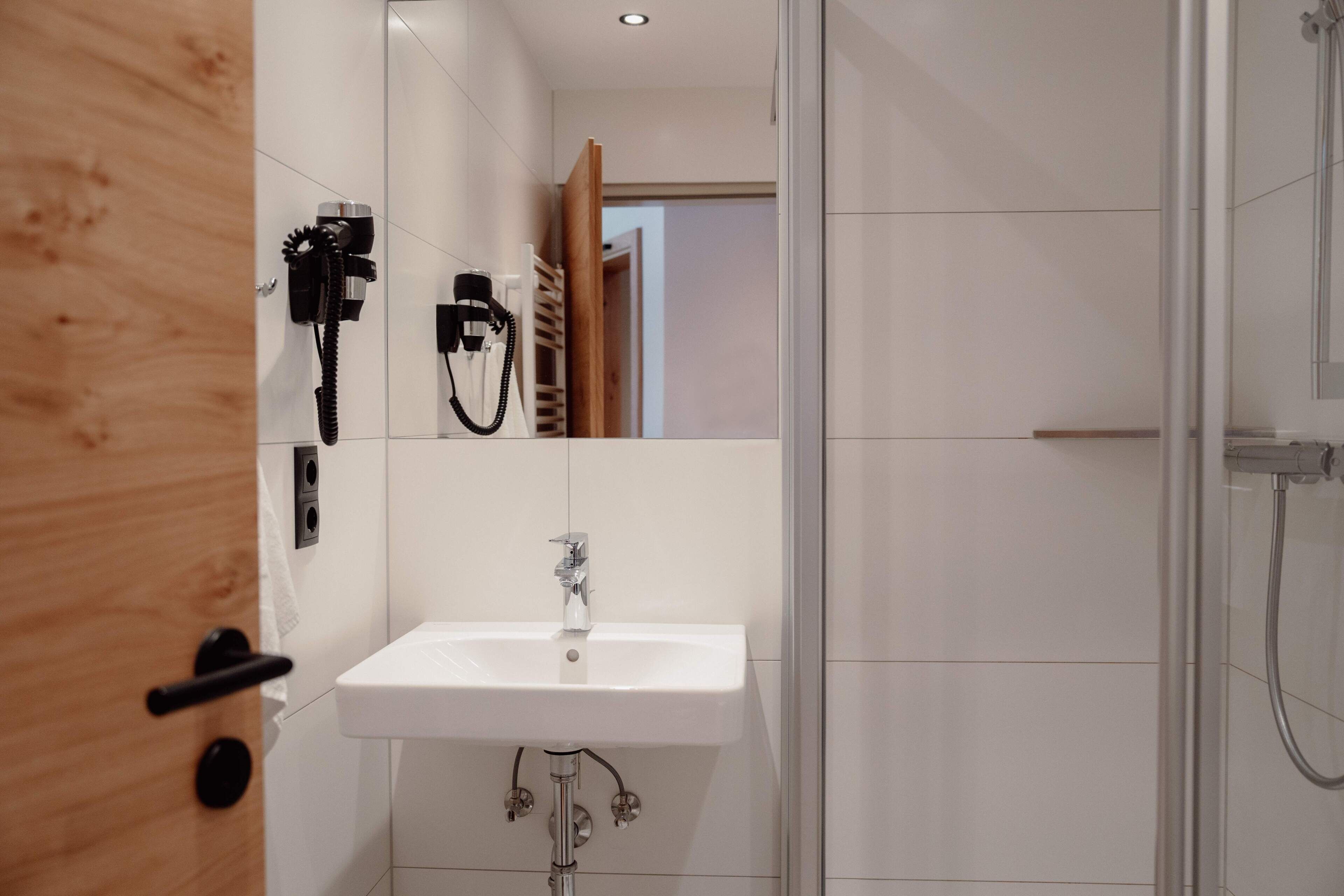 Un baño moderno con un lavamanos blanco, ducha y puerta de madera.