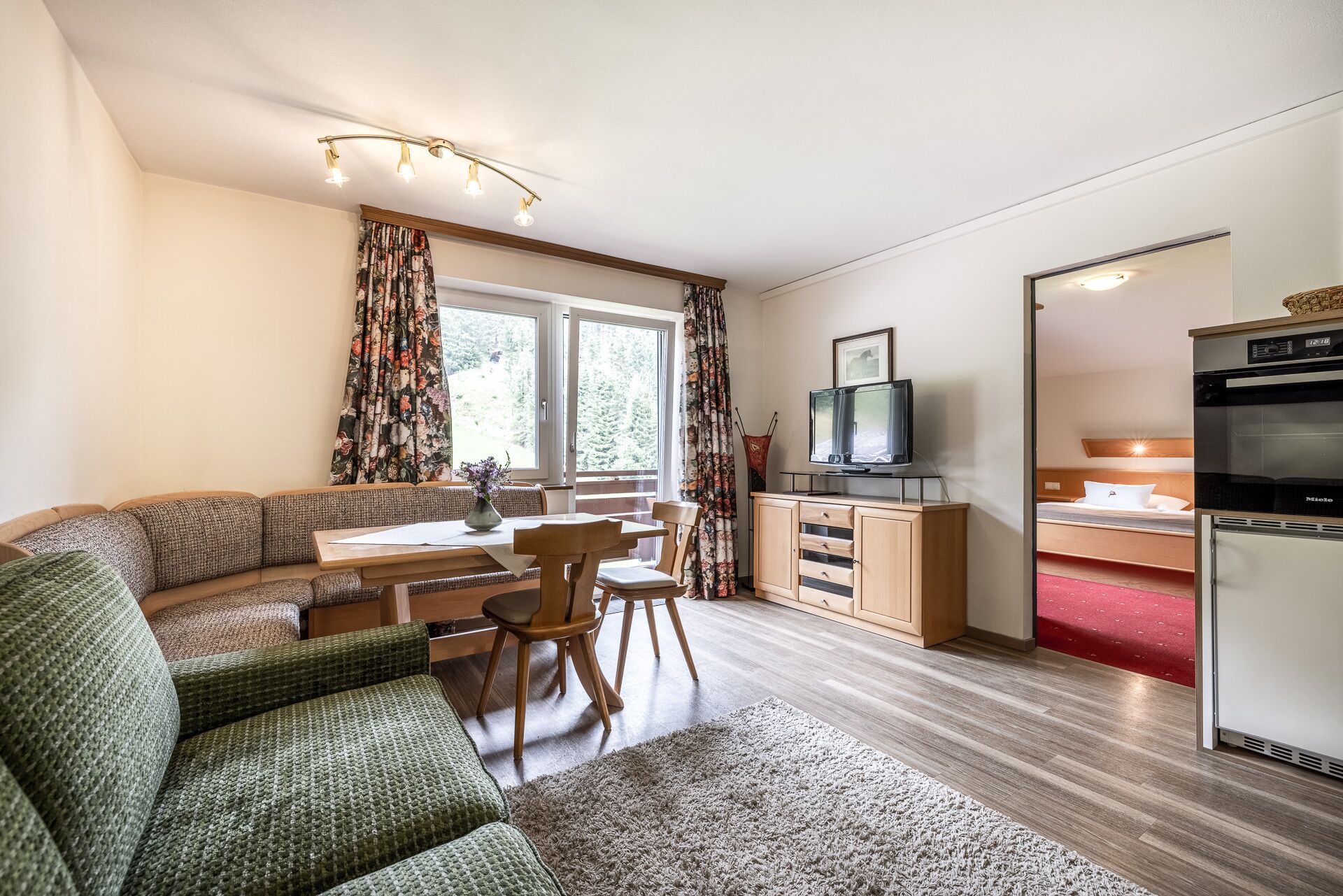 Un espacio habitable compacto con sofá, mesa de comedor, sillas, televisor y kitchenette.