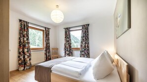A bedroom with a wooden bed, floral curtains, and a view of trees through the windows. - Das Filzmoos (Filzmoos)